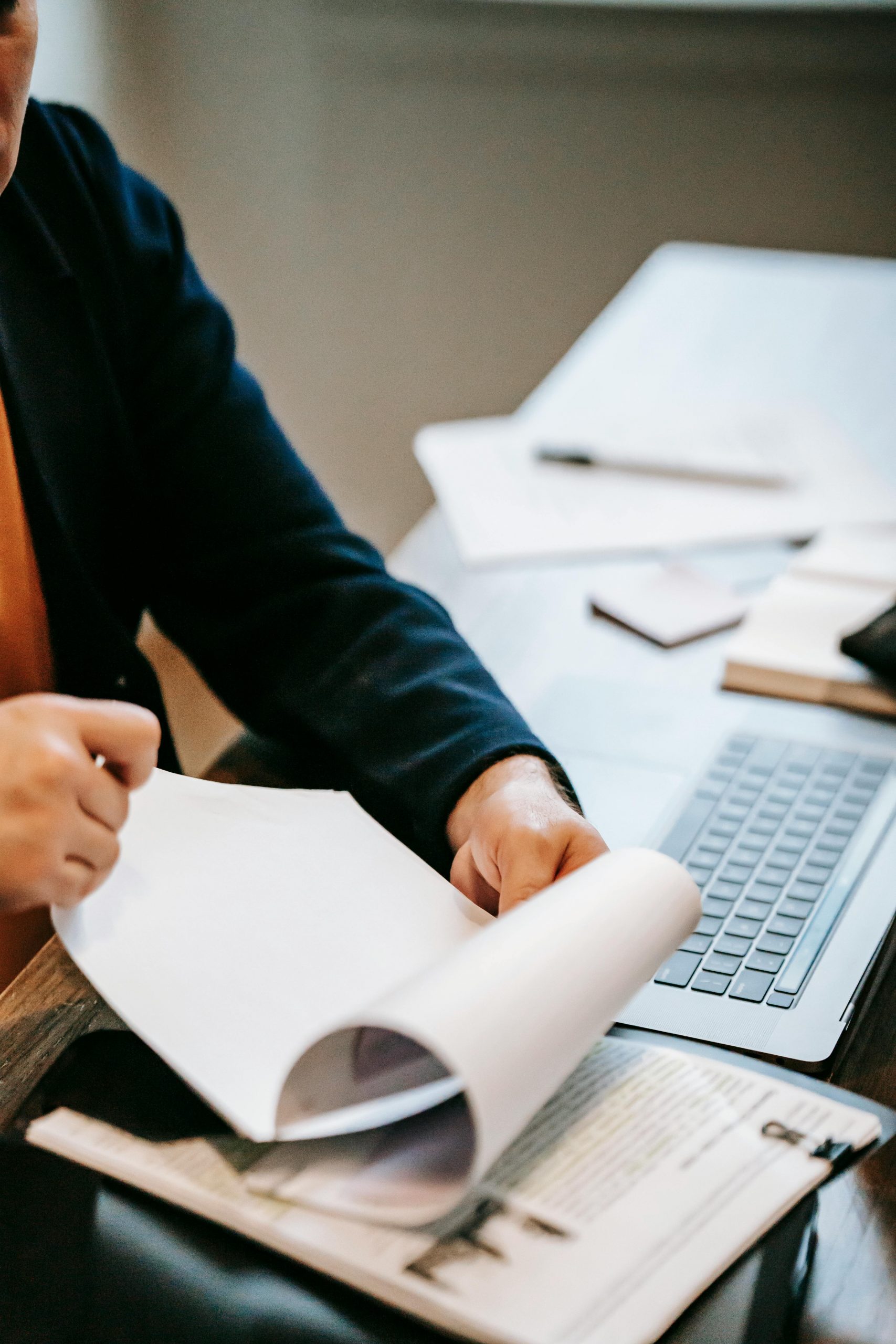 Man looking through files at a desk with a laptop and pen.